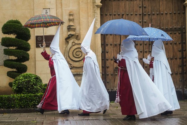 Penitents of the Brotherhood of The Judgment shelter from the rain under umbrellas on their way to a procession on the occasion of Holy Monday during the Holy Week in Cordoba, southern Spain, 25 March 2024. (Photo by Rafa Alcaide/EPA/EFE)