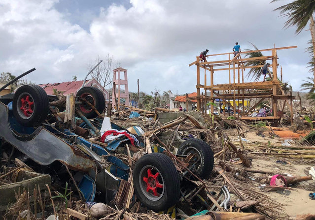 This photo taken on January 3, 2022, shows people constructing a new house (R) past an overturned vehicle and other debris in Burgos town, Siargao island, weeks after super Typhoon Rai devastated the island. (Photo by Roel Catoto/AFP Photo)
