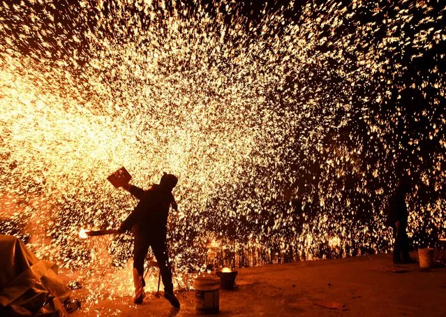 Blacksmiths throw molten metal to create a shower of sparks, on the eve of the Lantern Festival, which marks the end of Lunar New Year celebrations, at a park in Beijing on February 15, 2022. (Photo by Noel Celis/AFP Photo)
