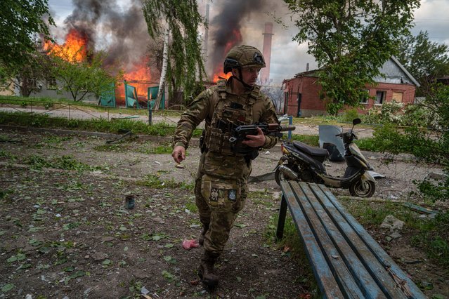 A police officer runs in front on burning house destroyed by a Russian airstrike in Vovchansk, Ukraine, on Saturday, May 11, 2024. (Photo by Evgeniy Maloletka/AP Photo)