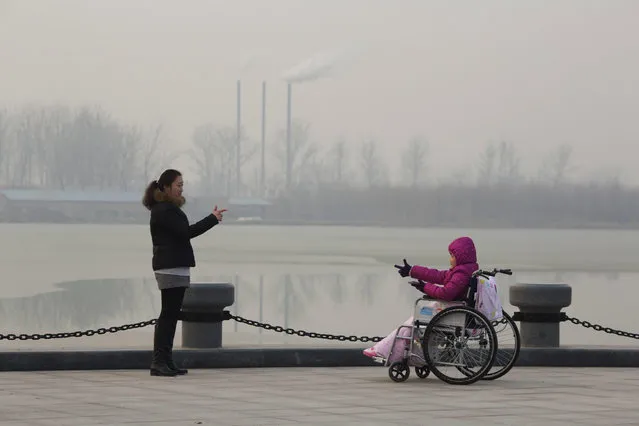 In this file photo taken Saturday, December 12, 2015, visitors to a park gestures at each other near chimneys spewing smoke in Beijing, China. Researchers say Tuesday, April 25, 2017 that China's conversion of coal into natural gas could prevent tens of thousands of premature deaths annually. But there's a catch: It also could undermine efforts to rein in greenhouse gas emissions. (Photo by Ng Han Guan/AP Photo)