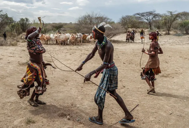 Female members of the Hammer tribe from the village of Turmi, situated in southern Ethiopia near the Kenyan border, accept a whipping by tribesmen as part of a ritual called the “bull jumping ceremony” that takes place during the passage of a young boy to adulthood, in Turmi, Ethiopia, 25 September 2019. The ceremony entails a young boy walking and jumping over seven bulls to become an adult while the tribe, who are mainly cattle ranchers, oversees the ceremony. The Hammer tradition wants women to have their hair coated with a mix of earth and butter that shall make them pretty while they dance during the ritual to give strenght to the young boy on his way to become an adult. In another part of the ceremony tribesmen with their faces painted whip women on demand to give courage to the adult initiate. (Photo by Stéphanie Lecocq/EPA/EFE)