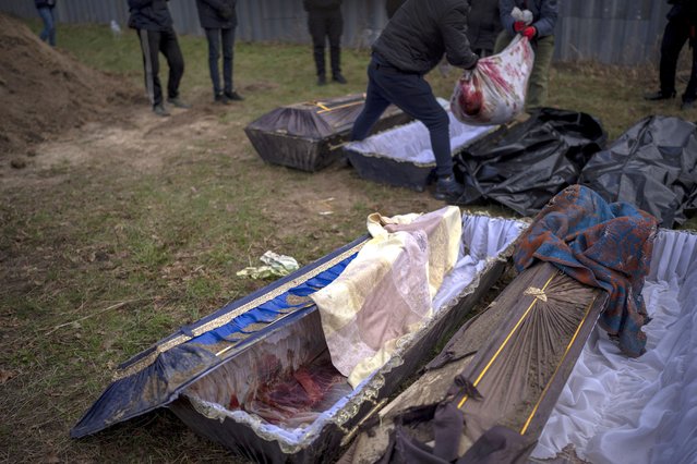 Volunteers put in a bag the body of a civilian killed by Russian army, after been removed from a mass grave, during an exhumation in Mykulychi, Ukraine on Sunday, April 17, 2022. (Photo by Emilio Morenatti/AP Photo)