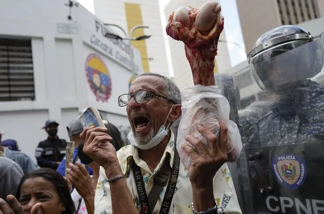 Roberto Carpio, 67, holds up an animal bone to symbolize that his monthly pension of about $30 dollars does not pay him enough to eat, during a protest demanding better pay for workers, pensioners and retirees in Caracas, Venezuela, Wednesday, April 6, 2022, as police block protesters from reaching the vice president's office. Pensioners have protested dozens of times across the country, and at the protests in the capital, some could be seen wearing broken shoes and worn clothes. (Photo by Ariana Cubillos/AP Photo)