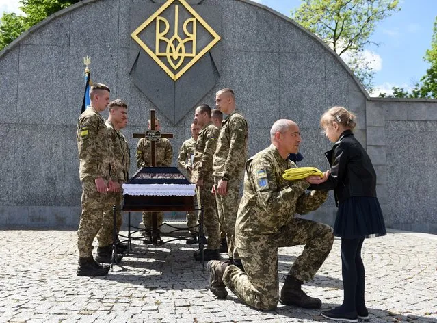 A serviceman offers the Ukrainian flag to the daughter of Yuriy Huk, a Ukrainian serviceman, killed during the Russian invasion of Ukraine, at his funeral service at the Saints Peter and Paul Garrison Church, in the western Ukrainian city of Lviv on May 16, 2022. (Photo by Yuriy Dyachyshyn/AFP Photo)