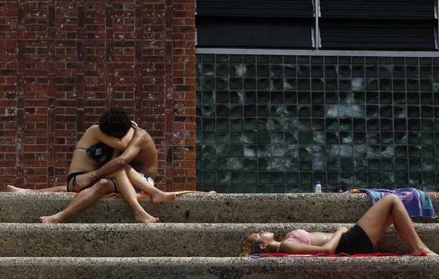 A couple embraces as another woman lies out in the sun on the steps next to the Astoria Park Pool in New York July 21, 2011. (Photo by Lucas Jackson/Reuters)