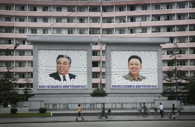 North Koreans are dwarfed against giant portraits of the late North Korean leaders Kim Il Sung and Kim Jong Il as they walk past an apartment building on Wednesday, June 22, 2016, in Wonsan, North Korea. (Photo by Wong Maye-E/AP Photo)