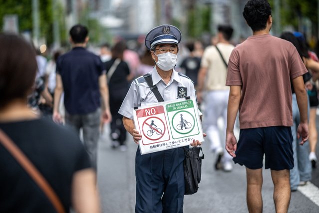 A security guard holds a no cycling sign in the pedestrian zone of Tokyo's Ginza district during the “Respect for the Aged Day” public holiday on September 16, 2024. (Photo by Philip Fong/AFP Photo)