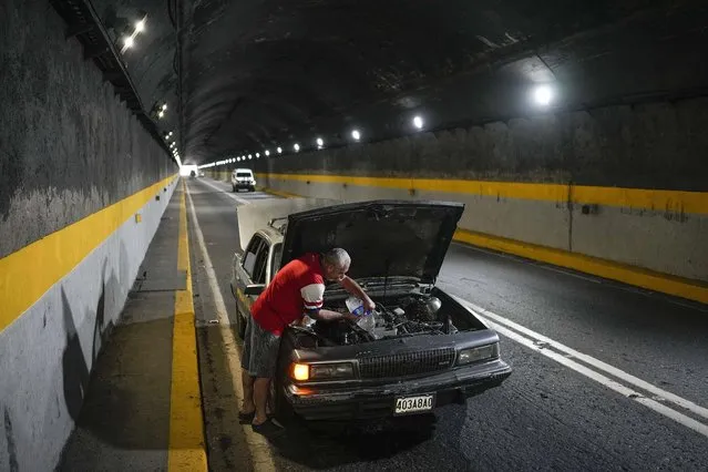 A man tries to cool down his overheating car by pouring water into the radiator, in one of the tunnels of the road that connects La Guaira with Caracas, Venezuela, Tuesday, April 19, 2022. Drivers try to coax a little more life out of aging vehicles in a country whose new car market collapsed and where few can afford to trade up for a better used one. (Photo by Matias Delacroix/AP Photo)
