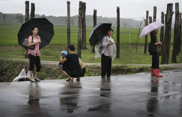 North Koreans shelter themselves from the rain as they wait for transportation along the road, Saturday, July 26, 2014 in the North Pyongan Province, North Korea. (Photo by Wong Maye-E/AP Photo)