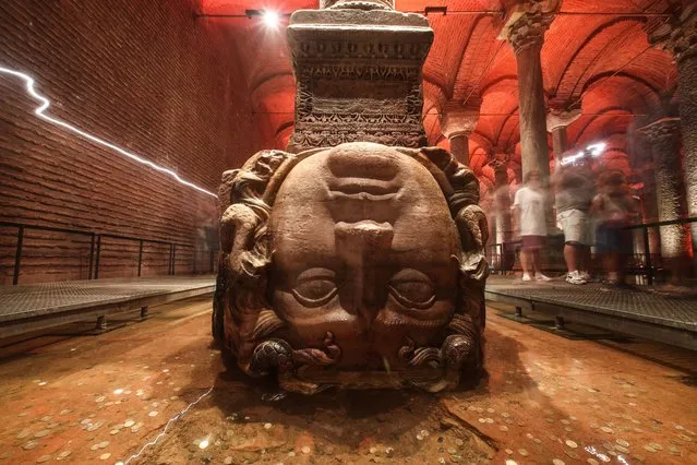 People walk behind the Medusa head in the Basilica Cistern in Istanbul, Turkey, 24 July 2022. The site has been restored by the Istanbul Metropolitan Municipality and is now open for visitors again. The Byzantine structure was commissioned by Emperor Justinian and built in 532. The underground Basilica, also called Underground Cistern, is the largest well preserved cistern in Istanbul, which rests on a total of 336 columns. According to historical texts, more than 7,000 slaves were involved in the construction of the cistern. (Photo by Sedat Suna/EPA/EFE)