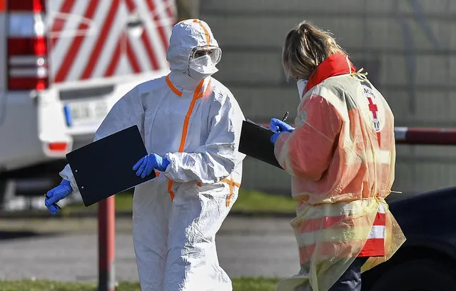 Workers of the fire department and the Red Cross take samples for coronavirus tests from car drivers at a mobile test station in Oberhausen, Germany, Tuesday, March 17, 2020. All public and private events are banned in Germany, clubs, bars restaurants and most shops are closed due to the virus outbreak. For most people, the new coronavirus causes only mild or moderate symptoms, such as fever and cough. For some, especially older adults and people with existing health problems, it can cause more severe illness, including pneumonia. (Photo by Martin Meissner/AP Photo)