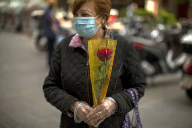 Maria, wearing a face mask and gloves, holds a rose as she queues to enter in a shop during Saint Jordi day, in Barcelona, Spain, Thursday, April 23, 2020 as the lockdown to combat the spread of coronavirus continues. (Photo by Emilio Morenatti/AP Photo)