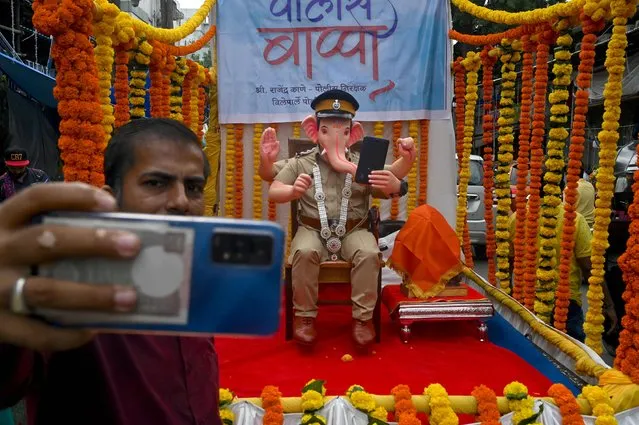A passerby takes a selfie with an idol of the elephant-headed Hindu God Lord Ganesh in the avatar of a policeman during 'Ganesh Chaturthi' festival in Mumbai on August 31, 2022. (Photo by Indranil Mukherjee/AFP Photo)
