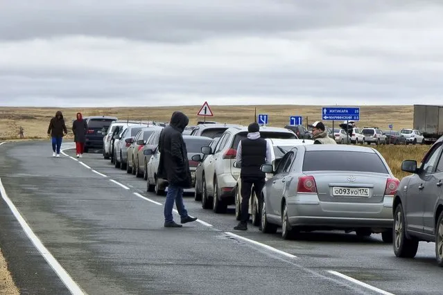 People walk next to their cars queuing to cross the border into Kazakhstan at the Mariinsky border crossing, about 400 kilometers (250 miles) south of Chelyabinsk, Russia, Tuesday, September 27, 2022. Officials say about 98,000 Russians have crossed into Kazakhstan in the week since President Vladimir Putin announced a partial mobilization of reservists to fight in Ukraine. (Photo by AP Photo/Stringer)