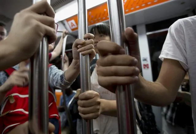 In this September 5, 2014, photo, commuters grasp the poles on a subway during the evening rush hour in Rome. On packed subways and crowded highways, billions of people participate in a short-distance worldwide population shift twice a day: the rhythmic ritual of the daily commute to and from work. (Photo by Alessandra Tarantino/AP Photo)