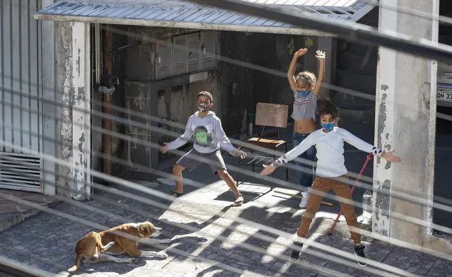 Children exercise from the rooftop of their building during and outdoor workout class imparted by physical trainer Ivan Nascimento for his neighbors during a quarantine imposed by the state government to help contain the spread of the new coronavirus in the Brasilandia neighborhood of Sao Paulo, Brazil, Sunday, May 17, 2020. (Photo by Andre Penner/AP Photo)