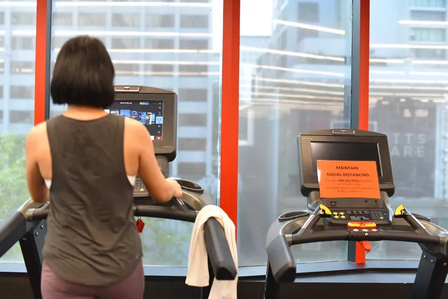 A sign that reads “maintain social distancing” is mounted on a vacant treadmill beside a woman at a fitness center Friday, June 19, 2020, in Singapore. Singaporeans now can wine and dine at restaurants, work out at the gym and get together with up to five people after most lockdown restrictions were lifted Friday. (Photo by Y.K. Chan/AP Photo)