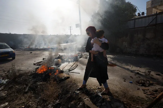 A woman carrying a child walks past a burning tire after Israeli forces killed Palestinians in an incident, in Jalazone refugee camp, in the Israeli-occupied West Bank October 3, 2022. (Photo by Mohamad Torokman/Reuters)