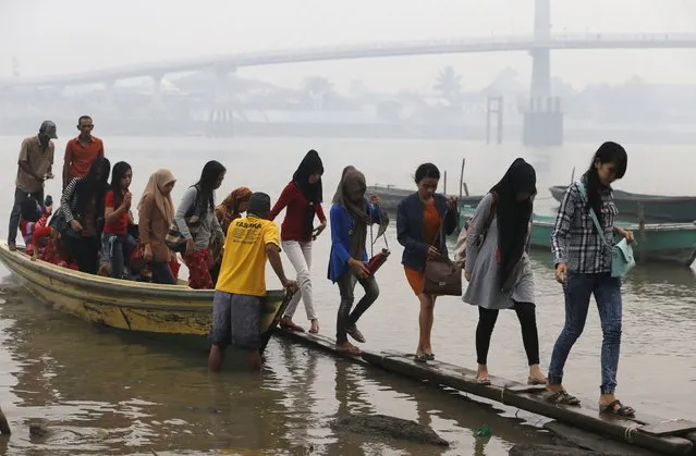 Workers walk on wooden planks as they disembark a boat after crossing Batanghari River in haze-shrouded Jambi, on the Indonesian island of Sumatra, September 17, 2015. A worsening haze across northern Indonesia, neighbouring Singapore and parts of Malaysia on Tuesday forced some schools to close and airlines to delay flights, while Indonesia ordered a crackdown against lighting fires to clear forested land. (Photo by Reuters/Beawiharta)