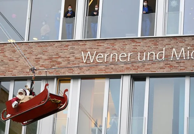 A firefighter dressed as Saint Nicholas abseils from the roof of a children's medical unit of a the UKE hospital to deliver presents to children in Hamburg, Germany on December 6, 2022. (Photo by Fabian Bimmer/Reuters)