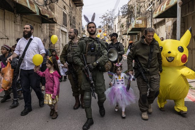 Israeli soldiers guard Jewish settlers wearing costumes as they celebrate the Jewish holiday of Purim during an annual parade in the occupied West Bank city of Hebron, Sunday, March 24, 2024. The Purim Jewish holiday commemorates the Jews' salvation from genocide in ancient Persia, as recounted in the biblical Book of Esther.(Photo by Heidi Levine for The Washington Post).