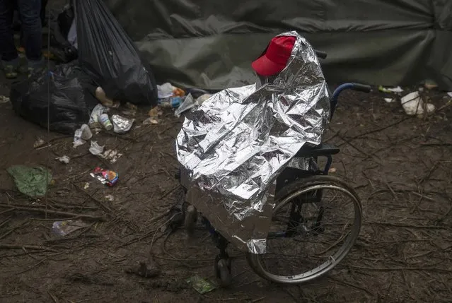 A migrant on a wheelchair protects himself from the rain near the border crossing with Croatia, near the village of Berkasovo, Serbia October 19, 2015. (Photo by Marko Djurica/Reuters)
