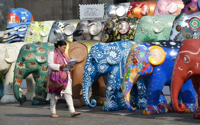 An Indian member of staff takes notes as she walks among elephant sculptures displayed as part of the Elephant Parade India initiative in Mumbai on February 25, 2018. The elephant sculptures will be displayed at prominent Mumbai locations for 3 weeks as part of what has become recognised as the world's biggest public art event - The Elephant Parade. After the display each elephant sculpture will be sold in an auction to raise funds for Asian elephant corridors and projects to address human-elephant-conflict throughout India. (Photo by Indranil Mukherjee/AFP Photo)