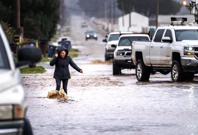 A woman braves the flooded streets alongside splashing trucks as an atmospheric river storm slams California in Salinas, California on Friday March 10, 2023. (Melina Mara/The Washington Post)
