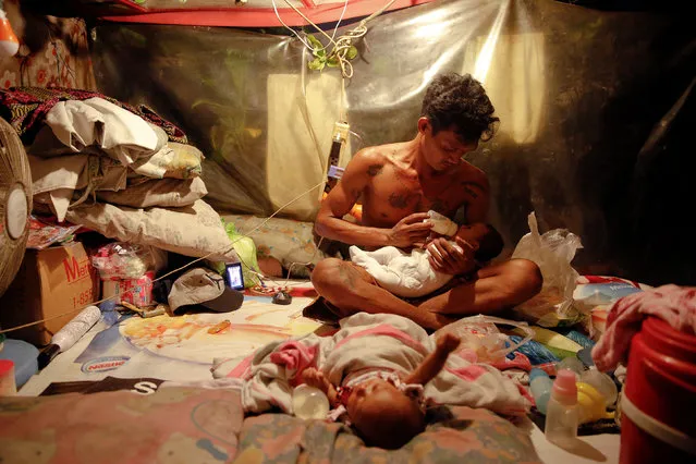 A man who lives with his family in a tent erected atop a tombstone, feeds his two-month old twins at the North Cemetery where many victims of country's war on drugs are buried in Manila, Philippines October 16, 2016. (Photo by Damir Sagolj/Reuters)