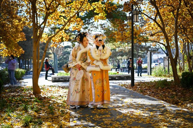 Two women wearing traditional clothes take a selfie as they walk along a pathway in Beijing on November 11, 2025. (Photo by Wang Zhao/AFP Photo)