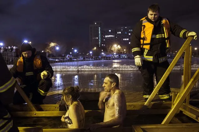 Russian woman and man bathe in the icy water to mark Epiphany as lifeguards watch over them in Moscow, Russia, late Sunday, January 18, 2015. The temperature in Moscow is 1 degrees C (34 degrees F). Thousands of Russian Orthodox Church followers plunged into icy rivers and ponds across the country to mark Epiphany, cleansing themselves with water deemed holy for the day. (Photo by Pavel Golovkin/AP Photo)