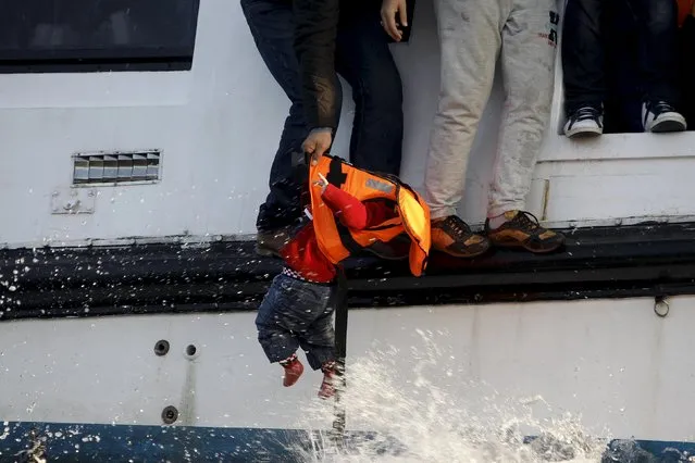 A refugee prepares to hand over a toddler to a volunteer lifeguard as a half-sunken catamaran carrying around 150 refugees, most of them Syrians, arrives after crossing part of the Aegean sea from Turkey on the Greek island of Lesbos, October 30, 2015. (Photo by Giorgos Moutafis/Reuters)
