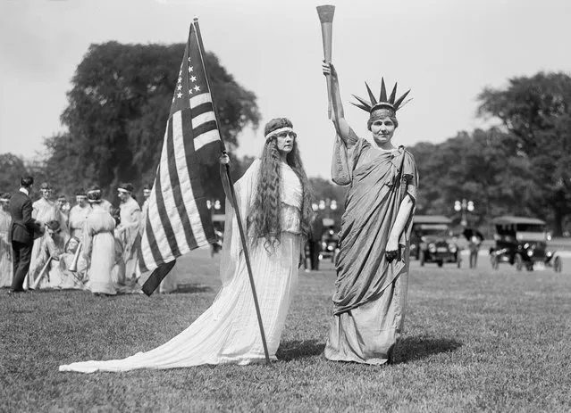 A woman holding the American flag stands witha women in Statue of Liberty costume during Fourth of July celebrations at the Ellipse, Washington D.C.,1919. (Photo by Harris & Ewing/GHI/Universal History Archive via Getty Images)