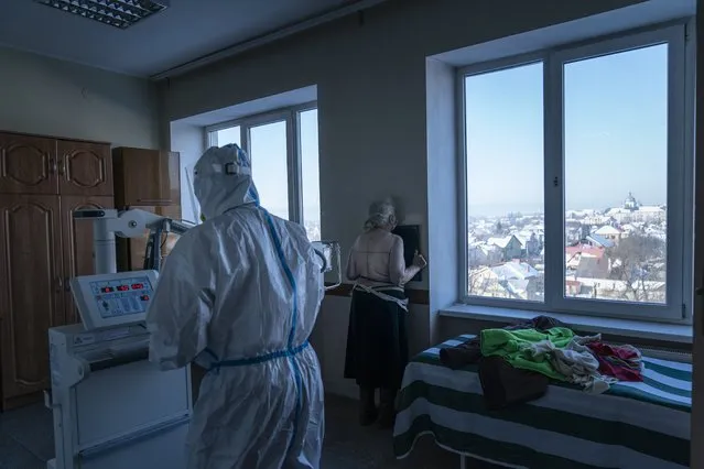 A medic wearing a special suit to protect against coronavirus, back to a camera prepares a patient with coronavirus for a lung X-ray at a hospital in Kolomyia, western Ukraine, Tuesday, February 23, 2021. (Photo by Evgeniy Maloletka/AP Photo)