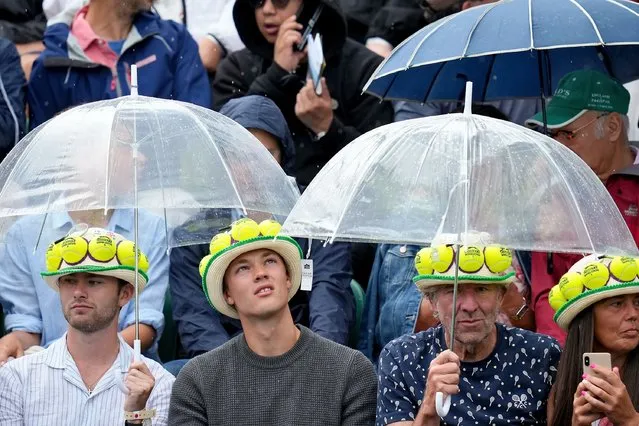 Spectators shelter under umbrellas on court 3 as it starts to rain during the singles match between Denmark's Holger Rune and Britain's George Loffhagen on day two of the Wimbledon tennis championships in London, Tuesday, July 4, 2023. (Photo by Kirsty Wigglesworth/AP Photo)