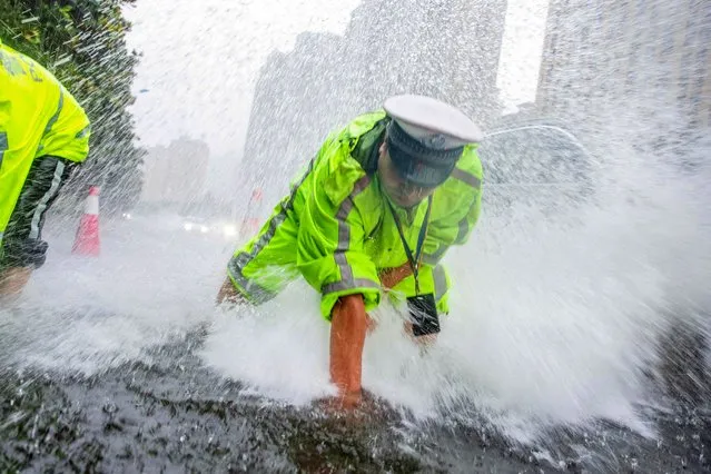 A traffic police officer drains water on a street during a rainfall in Nantong, in China's eastern Jiangsu province on July 7, 2023. (Photo by AFP Photo/China Stringer Network)