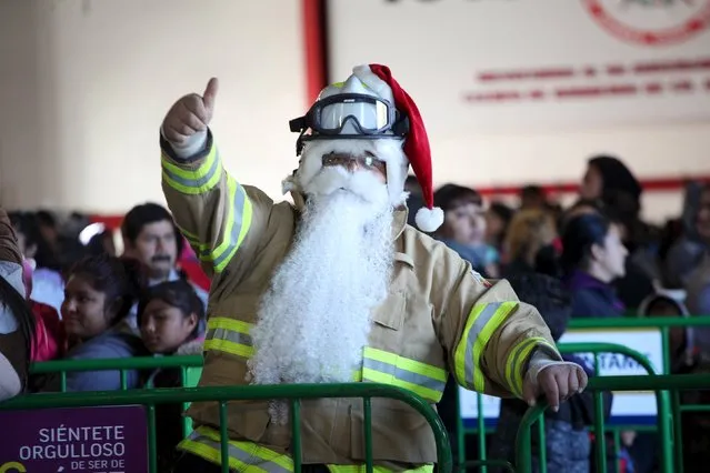 A firefighter, wearing a beard and a Santa Claus hat, gestures during the annual gift-giving event organised by firefighters in Ciudad Juarez, Mexico, December 24, 2015. The firefighters from Ciudad Juarez collect donated toys throughout the year for Christmas and hand them out to poor children on Christmas eve. (Photo by Jose Luis Gonzalez/Reuters)