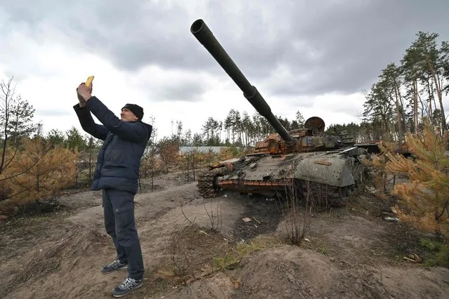 A man takes a selfie as he stands in front of a destroyed Russian tank in the vilage of Andriivka, in the Kyiv region on April 17, 2022. Russia invaded the Ukraine on February 24, 2022. (Photo by Sergei Supinsky/AFP Photo)