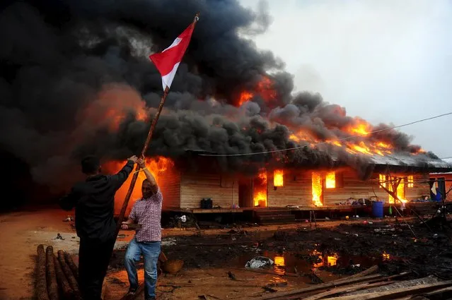 Two men remove the Indonesian flag as the compound of the Gafatar sect burns after being set on fire by local villagers, at Antibar village in Mempawah Regency, Indonesia West Kalimantan Province, January 19, 2016 in this photo taken by Antara Foto. (Photo by Jessica Helena Wuysang/Reuters/Antara Foto)