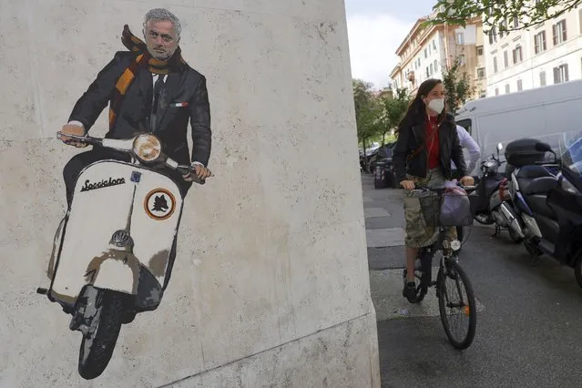 A woman rides her bicycle near a mural depicting coach Jose' Mourinho riding a Vespa scooter adorned with the Roma soccer team symbol and wearing a red and yellow scarf in the Testaccio neighborhood of Rome, Friday, May 7, 2021. Mourinho, that most outspoken of soccer coaches, will take over next season at Roma, the team with some of the most outspoken fans in Italy. Having memorably declared himself the “Special One” when he first reached the big time at Chelsea in 2004, one of Mourinho's most famous phrases in Italy was uttered at the expense of Roma five years later. (Photo by Gregorio Borgia/AP Photo)