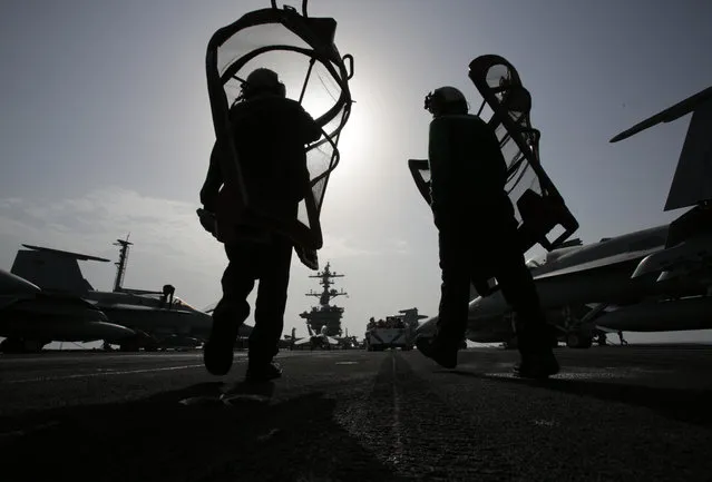 U.S. sailors carry equipment on the flight deck of the USS Carl Vinson aircraft carrier in the Persian Gulf, Thursday, March 19, 2015. (Photo by Hasan Jamali/AP Photo)