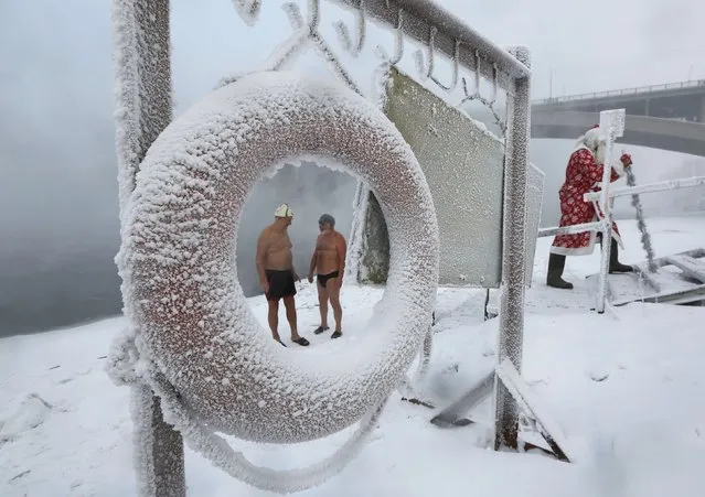 A man dressed as Ded Moroz, the Russian equivalent of Santa Claus, walks near Ivan Abrosimov, 80, (L) and Nikolay Bocharov, 78, members of the Cryophile amateurs winter swimmers club, who speak after taking a bath in the icy waters of the Yenisei River during the celebrations for the upcoming Christmas and New Year, with the air temperature at about minus 34 degrees Celsius (minus 29.2 degrees Fahrenheit), in Krasnoyarsk, Russia, December 24, 2016. (Photo by Ilya Naymushin/Reuters)