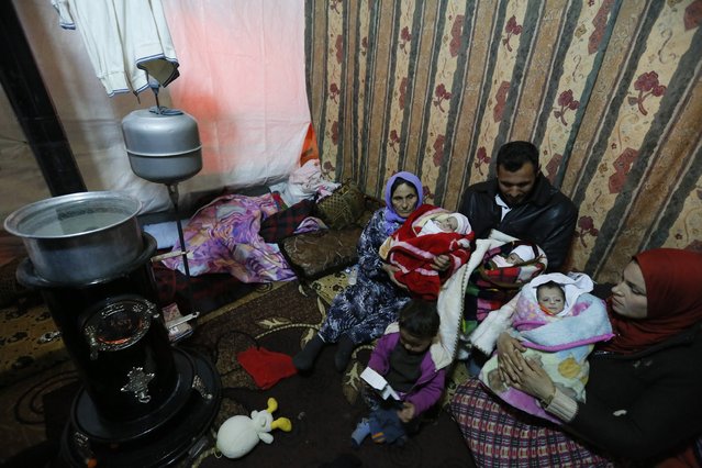 Syrian refugee Saleh al Mohammed (C) holds his 18 days old son Khaled, as his mother (L) and sister (R) hold his brothers Ahmed and Riyad at their tent in a refugee camp near Zahle town in the Bekaa Valey January 18, 2015. The mother of the triplets, Amal Asad al Jassem, 17, died in a nearby hospital while giving birth on January 1, 2015. (Photo by Jamal Saidi/Reuters)