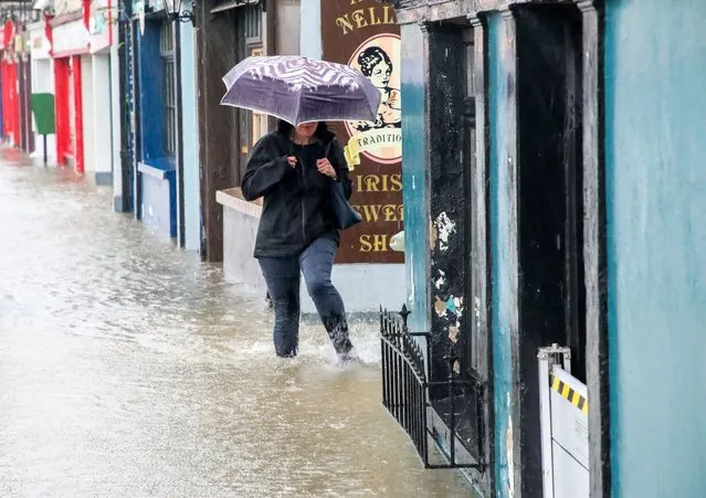 A woman wades throug a flooded Main Street as she makes her way to work in Carrigaline, Co. Cork, Ireland on October 18, 2023. (Photo by David Creedon/The Irish Times)