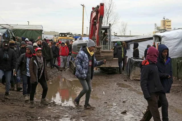 Migrants walk in the mud near a crane operated by volunteers that makes its way along a path in the southern part of a camp for migrants called the “jungle”, in Calais, northern France, February 23, 2016. (Photo by Pascal Rossignol/Reuters)