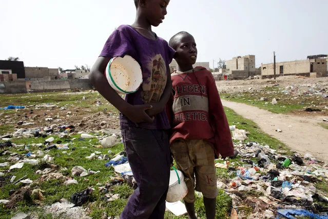 Two unidentified young boys, Talibe students, walk in a field littered with garbage, holding the buckets from which they ate a lunch of rice and fish in Guediawaye, a suburb on the outskirts of of Dakar, Senegal, Monday, April 20, 2015. They need to find more food before returning to school so they don't get beaten. (Photo by Jane Hahn/AP Photo)