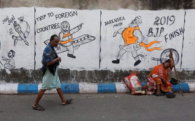 A man walks past a woman who sits by a wall with graffiti that mocks Indian politicians ahead of the general election in Kolkata, April 1, 2019. (Photo by Rupak De Chowdhuri/Reuters)