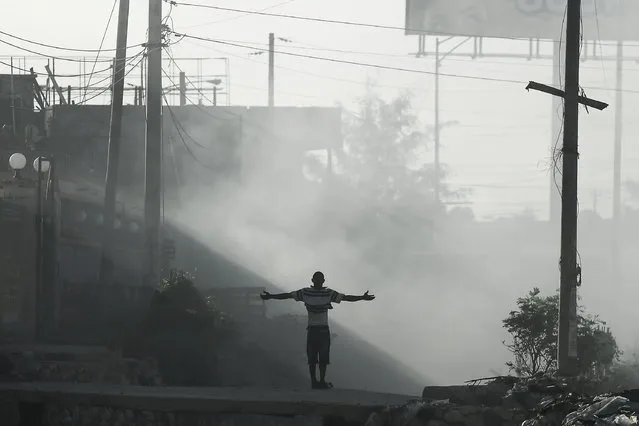 A man spreads his arms apart in smoke created by burning garbage in Port-au-Prince, Haiti, Tuesday, October 26, 2021, during a general strike and fuel shortages. Worker unions along with residents called for a general strike to demand the end of kidnappings, violence and insecurity in the streets. (Photo by Matias Delacroix/AP Photo)