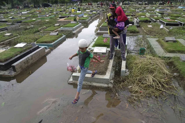 A family navigates the puddles at a flooded cemetery as they visit the grave of a relative ahead of the Muslim holy fasting month of Ramadan in Jakarta, Indonesia, Friday, March 8, 2024. Prior Ramadan, the holiest month in Islamic calendar, Indonesian Muslims followed local tradition to visit cemeteries to pray for their deceased loved ones. (Photo by Dita Alangkara/AP Photo)